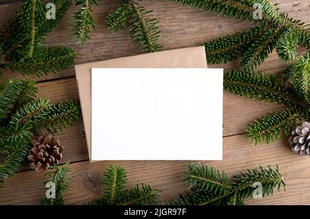 Weihnachten 7x5 Karte Mockup Vorlage mit Umschlag mit Tannenzweigen und Weihnachtsdekor auf Holzhintergrund. Design-Element für Weihnachten und Neujahr CO Stockfoto