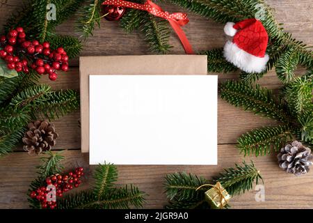Weihnachten 7x5 Karte Mockup Vorlage mit Umschlag mit Tannenzweigen und Weihnachtsdekor auf Holzhintergrund. Design-Element für Weihnachten und Neujahr CO Stockfoto