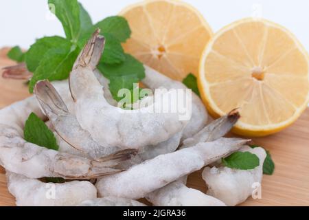 Gefrorene, rohe Garnelen, geschält auf einem Holzschneidebrett mit Kräutern und Zitrone. Stockfoto