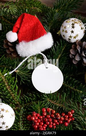 Weihnachtliche runde weiße Tag-Mockup mit weißer Kordel, Nahaufnahme auf natürlichem Tannenzweig, mit Zapfen und Weihnachtsdekoration, Weihnachtsverkauf-Konzept. Bl Stockfoto