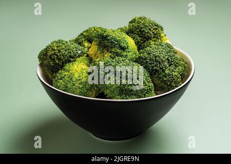 Rohe Brokkoli floriert in einer schwarzen Schüssel auf einem Rasen grün gefärbten Hintergrund. Vegetarische Vitamingerichte. Kalorienarme antioxidative Detox Diät Konzept. Stockfoto