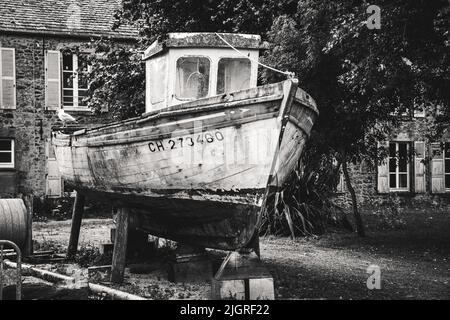 Eine Graustufenaufnahme eines alten Holzbootes auf dem Hinterhof eines Hauses Stockfoto