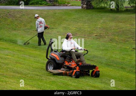 Zwei Männer mit einem Rasenmäher und -Trimmen mit einem Rasentraktor und Unkrautfräser Stockfoto