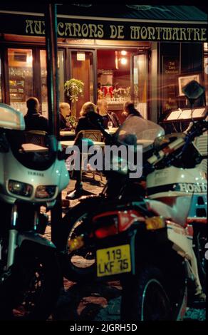 Ihre Motorräder parkten an der Bordsteinkante, die Gäste essen auf dem Bürgersteig vor einem Café im Pariser Viertel Montmartre. Stockfoto