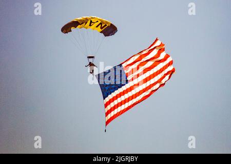 Ein Mitglied der US Navy Leap Frogs Flag Jump entrollt eine gewichtete US-Flagge, während es anlässlich des 4.. Juli über Huntington Beach, CA, parasiliert. Stockfoto