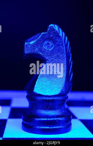 Schwarzer Ritter steht allein auf einem Schachbrett. Armee von einem. Selektiver Fokus. Dunkler Hintergrund. Neonblaues Licht vor der Komposition. Selektiver Fokus Stockfoto