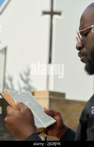 Nahaufnahme eines afroamerikanischen Predigers mit offenen Bibelversen, während er über ihre Bedeutung spekuliert oder sich auf eine Predigt vorbereitet Stockfoto