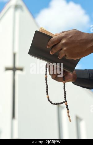 Hände eines schwarzen Mannes, der die Heilige Bibel in Lederhülle und hölzernen Rosenkranzperlen aufhält, während er das Evangelium liest und zum Herrn betet Stockfoto