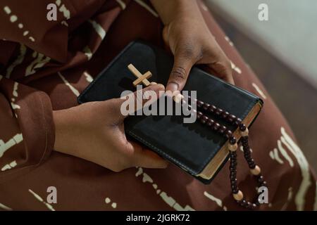 Hände von jungen afroamerikanischen Gemeindemitgliedern der katholischen oder evangelischen Kirche, die Bibel und Rosenkranz während der Predigt oder des Gebets halten Stockfoto