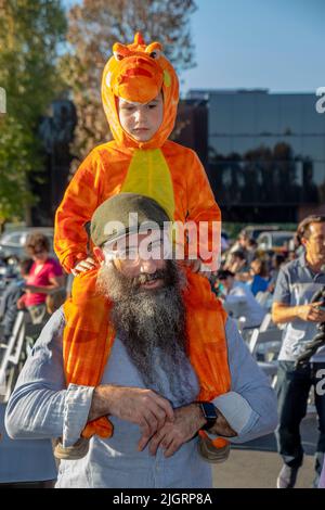 Der Sohn eines orthodoxen jüdischen Vaters ist bei einer Hanukkah-Feier im Freien in Newport Beach, CA, in ein Drachenkostüm gekleidet. Stockfoto