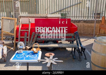 Limoux Aude Frankreich. 07.12.22 helle Flohmarkt-Szene, Holzbank, rotes Brocante-Schild mit weißem Schriftzug. Radweg-Ikonentisch. Ein Weinfass. S Stockfoto