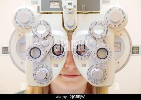 Ein männlicher Augenarzt überprüft das Augenlicht eines Mädchens mit einem Phoropter. Sehbehandlung. Stockfoto