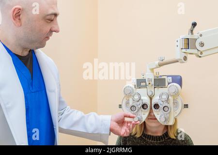 Ein männlicher Augenarzt überprüft das Augenlicht eines Mädchens mit einem Phoropter. Sehbehandlung. Stockfoto