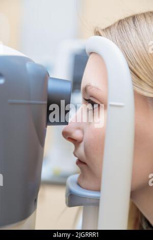 Ein junges Mädchen an der Rezeption des Augenarztes überprüft ihr Sehvermögen an einem speziellen Apparat. Nahaufnahme. Stockfoto