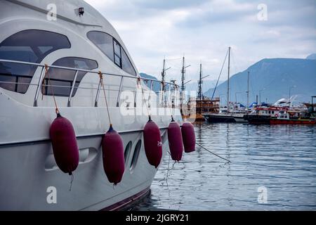 Schöne moderne weiße Yacht ist am Seebrücke vertäut. Yacht und Schlepper stehen auf dem Pier im Meer. Berge im Hintergrund. Stockfoto