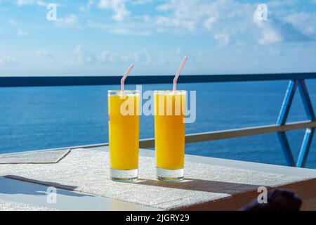 Zwei Gläser Orange sitzen auf einem Tisch in einem Café am Meer in einem Badeort. Blaues Meer im Hintergrund, sonniger Sommertag. Stockfoto