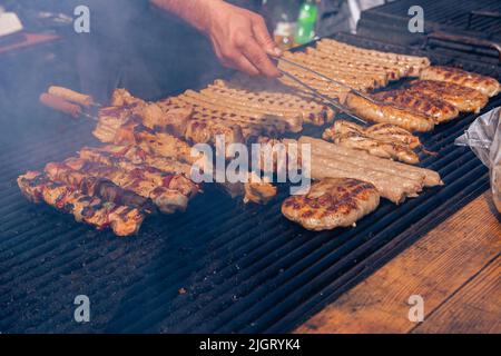 Barbecue auf dem Straßenmarkt. Nahaufnahme des Kochens von gegrillten Fleischgerichten an einem sonnigen Tag. Shish Kebab, Kebab, Fleischbällchen. Stockfoto