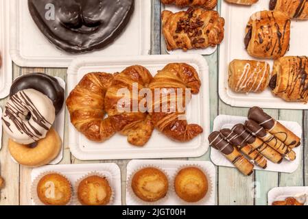 Set aus frisch gebackenen Süßprodukten, Schokoladenpalmen, verschiedenen Donuts, Buttercroissants, gefüllten Neapolitanen und Muffins Stockfoto