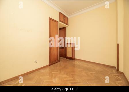 Leeres Schlafzimmer mit Fischgrätboden, hellgelb gestrichenen Wänden und eingebautem Kleiderschrank mit Holztür Stockfoto