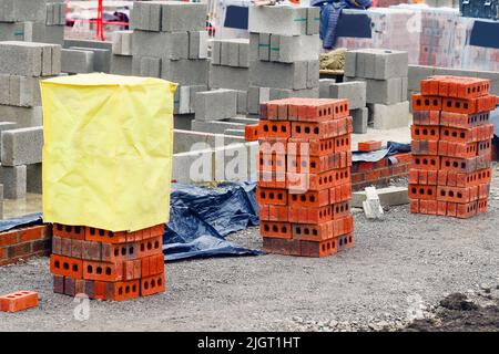 Rote Steine und Betonblöcke, die auf der Baustelle geliefert und neben dem Arbeitsort für Maurer aufgestellt wurden Stockfoto