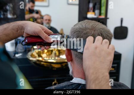 Ein alter Mann, der in einem Friseurladen einen Haarschnitt von einem Meister genießt. Ein alter Mann bekommt einen stylischen Haarschnitt Stockfoto