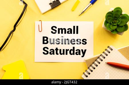 Text Small Business Saturday in Notebook auf weißem Tisch mit Office-Tools Stockfoto