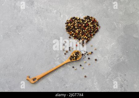 Mischung aus Pfefferkörnern in Herzform isoliert auf weißem Hintergrund. Mit Holzlöffel. Stockfoto