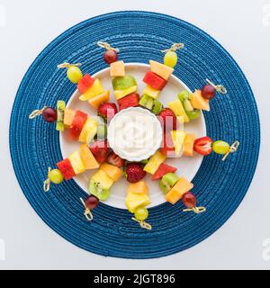 Eine runde Platte mit frischen Obstspießen und Joghurt-Dip in der Mitte. Stockfoto