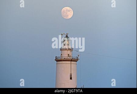 Malaga, Spanien. 12.. Juli 2022. Der Vollmond wird über dem Leuchtturm von Malaga aufsteigen sehen. Der zweite Supermond, bekannt als „Hirscher-Supermond“, wird in der Nacht vom 12. Auf den 13. Juli zu sehen sein. Der Supermond wird aufgrund seiner Nähe zur Erde der größte Supermond des Jahres sein. Kredit: SOPA Images Limited/Alamy Live Nachrichten Stockfoto