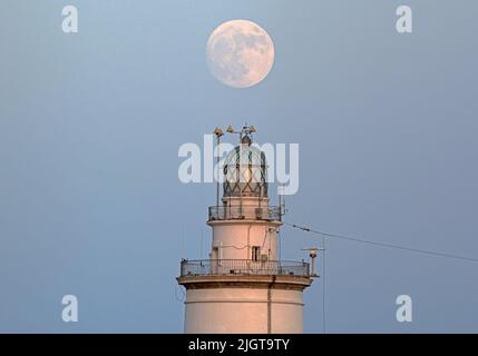 Malaga, Spanien. 12.. Juli 2022. Der Vollmond wird über dem Leuchtturm von Malaga aufsteigen sehen. Der zweite Supermond, bekannt als „Hirscher-Supermond“, wird in der Nacht vom 12. Auf den 13. Juli zu sehen sein. Der Supermond wird aufgrund seiner Nähe zur Erde der größte Supermond des Jahres sein. Kredit: SOPA Images Limited/Alamy Live Nachrichten Stockfoto