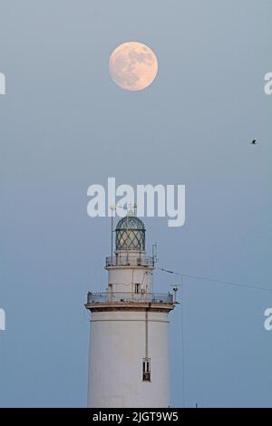 Malaga, Spanien. 12.. Juli 2022. Der Vollmond wird über dem Leuchtturm von Malaga aufsteigen sehen. Der zweite Supermond, bekannt als „Hirscher-Supermond“, wird in der Nacht vom 12. Auf den 13. Juli zu sehen sein. Der Supermond wird aufgrund seiner Nähe zur Erde der größte Supermond des Jahres sein. Kredit: SOPA Images Limited/Alamy Live Nachrichten Stockfoto