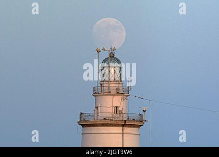 Malaga, Spanien. 12.. Juli 2022. Der Vollmond wird über dem Leuchtturm von Malaga aufsteigen sehen. Der zweite Supermond, bekannt als „Hirscher-Supermond“, wird in der Nacht vom 12. Auf den 13. Juli zu sehen sein. Der Supermond wird aufgrund seiner Nähe zur Erde der größte Supermond des Jahres sein. Kredit: SOPA Images Limited/Alamy Live Nachrichten Stockfoto