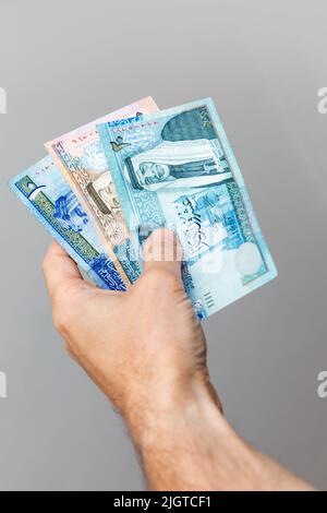 Männliche Hand mit jordanischen Dinar-Banknoten über grauem Wandhintergrund, vertikales Foto Stockfoto