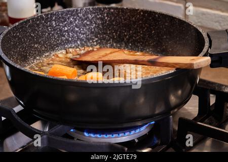 Karotten werden in einer Pfanne auf dem Gasherd gebraten, um geschmorten Fisch mit Pilzen und Kartoffeln zu machen Stockfoto