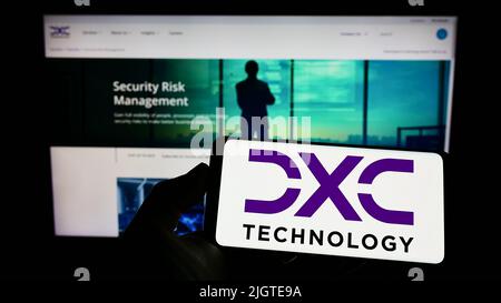 Person, die Mobiltelefon mit dem Logo der amerikanischen IT-Beratungsfirma DXC Technology Company auf dem Bildschirm vor der Webseite hält. Konzentrieren Sie sich auf die Telefonanzeige. Stockfoto