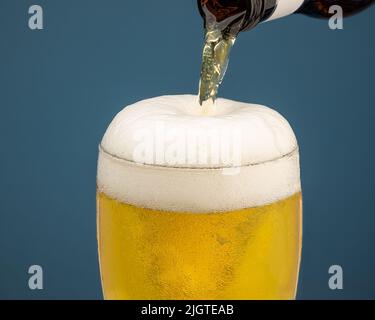 Kaltes Bier wird in ein Glas gegossen, Schaumkopf über der Oberseite des Glases Stockfoto