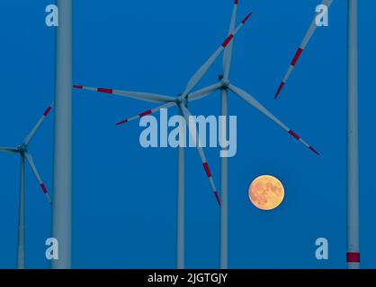 Sieversdorf, Deutschland. 12.. Juli 2022. Der Mond, der zu 95 Prozent sichtbar und zunehmend wird, leuchtet kurz nach Sonnenuntergang gelblich am Himmel zwischen Windenergieanlagen. In der Nacht des 13. Juli 2022 kann ein super Vollmond am Himmel gesehen werden, wenn die Sicht gut ist. Bei Mondaufgang gegen 10 Uhr wird sich der Erdsatellit 357.517 Kilometer von der Erde entfernt befinden. Trotz dieser Distanz wird es der größte Supermond des Jahres sein. Quelle: Patrick Pleul/dpa/Alamy Live News Stockfoto