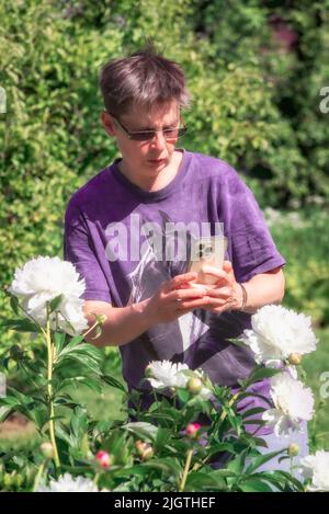 Frau fotografiert Pfingstrosen-Blumen auf ihrem Smartphone Stockfoto