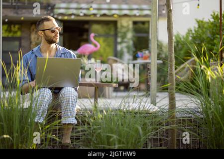 Der Mann arbeitet auf dem Laptop, während er im Hinterhof sitzt Stockfoto