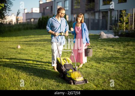 Junge Familie kümmert sich am Sommerabend um Rasen Stockfoto