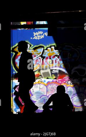 London, England, Großbritannien. Silhoutes von Menschen in der South Bank Undercroft (Lieblings-Skateboarding-Veranstaltungsort) gegen Graffiti im Hintergrund Stockfoto