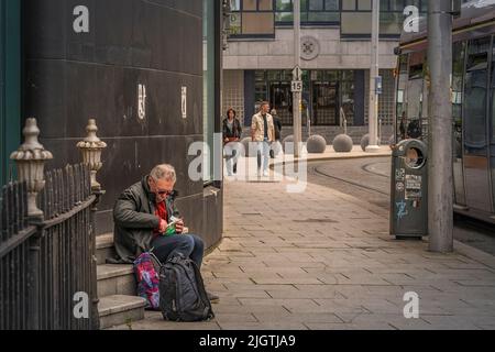 Ein älterer Mann rollt eine Zigarette auf der Seite eines Gebäudes. Dublin. Irland. Stockfoto