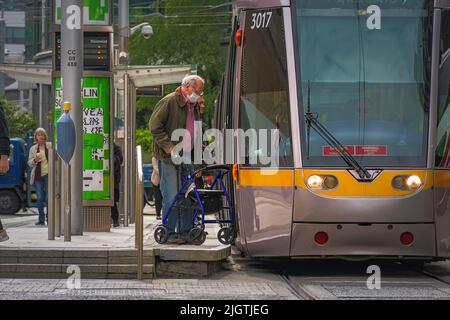 Ein älterer Mann mit Gehhilfe besteigen die Straßenbahn an der Haltestelle Busaras Luas. Dublin, Irland. Stockfoto