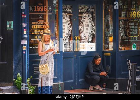 Mädchen bleiben direkt vor dem Pub mit Zigaretten und schauen sich ihre Handys an. Porter House Pub, Parliament Street. Dublin. Irland. Stockfoto