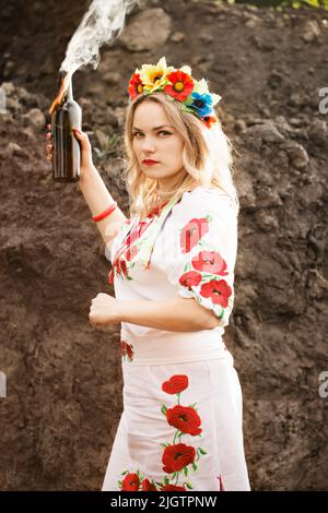 Ein Mädchen in einem ukrainisch-nationalen gestickten Kleid mit einem Molotow-Cocktail in den Händen, ein Symbol der Ukraine, die sich gegen die russische Invasion verteidigt Stockfoto