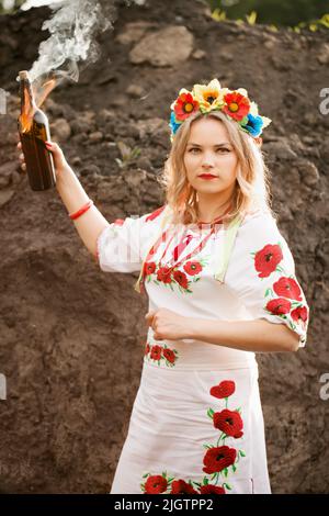 Ein Mädchen in einem ukrainisch-nationalen gestickten Kleid mit einem Molotow-Cocktail in den Händen, ein Symbol der Ukraine, die sich gegen die russische Invasion verteidigt Stockfoto