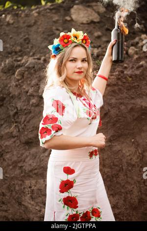 Ein Mädchen in einem ukrainisch-nationalen gestickten Kleid mit einem Molotow-Cocktail in den Händen, ein Symbol der Ukraine, die sich gegen die russische Invasion verteidigt Stockfoto