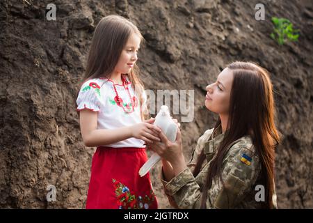 Eine Militärfrau überreichte einem kleinen ukrainischen Mädchen eine weiße Taube, das Konzept des Friedens in der Ukraine Stockfoto