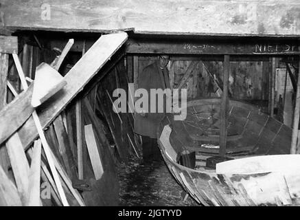 Geschrieben auf der Rückseite: '4.' Die Bilderserie aus einer holländischen Kleinbootrunde 0908-0930. Ein Mann, der an einem Bootsrumpf in einem Bootsschuppen steht. Stockfoto