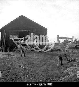 Ein Boot wird gebaut, Spant und Kiel sind eingestellt. Es ist auf einer Ziege montiert. An der Tür des Hauses, wo das Boot steht, befindet sich eine Plakatwand (Östgöta Haus). Stockfoto